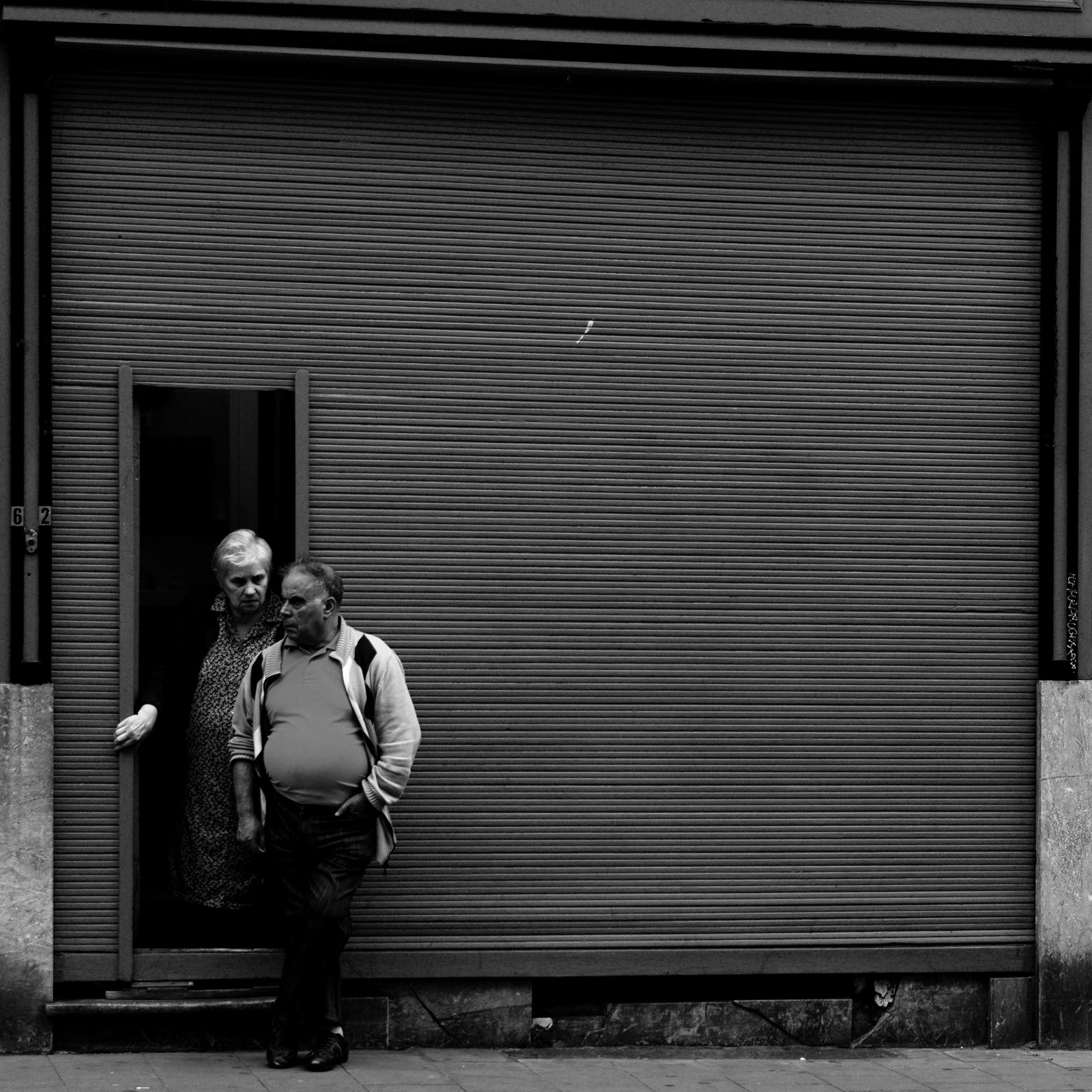 Couple standing beside a small doorway in a large shuttered facade.