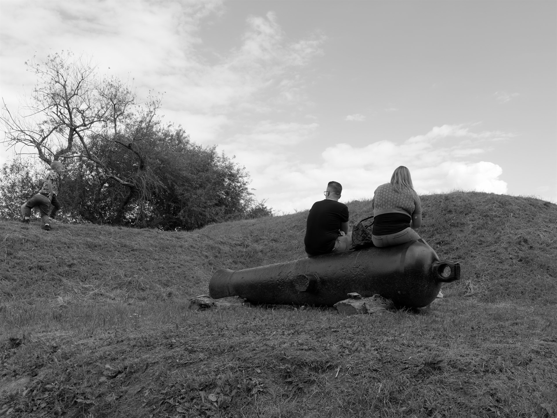 Couple sitting on an old cannon with a child on the slope.