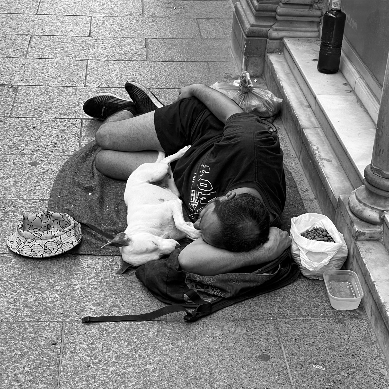 Man lying on the pavement with a dog resting against him.