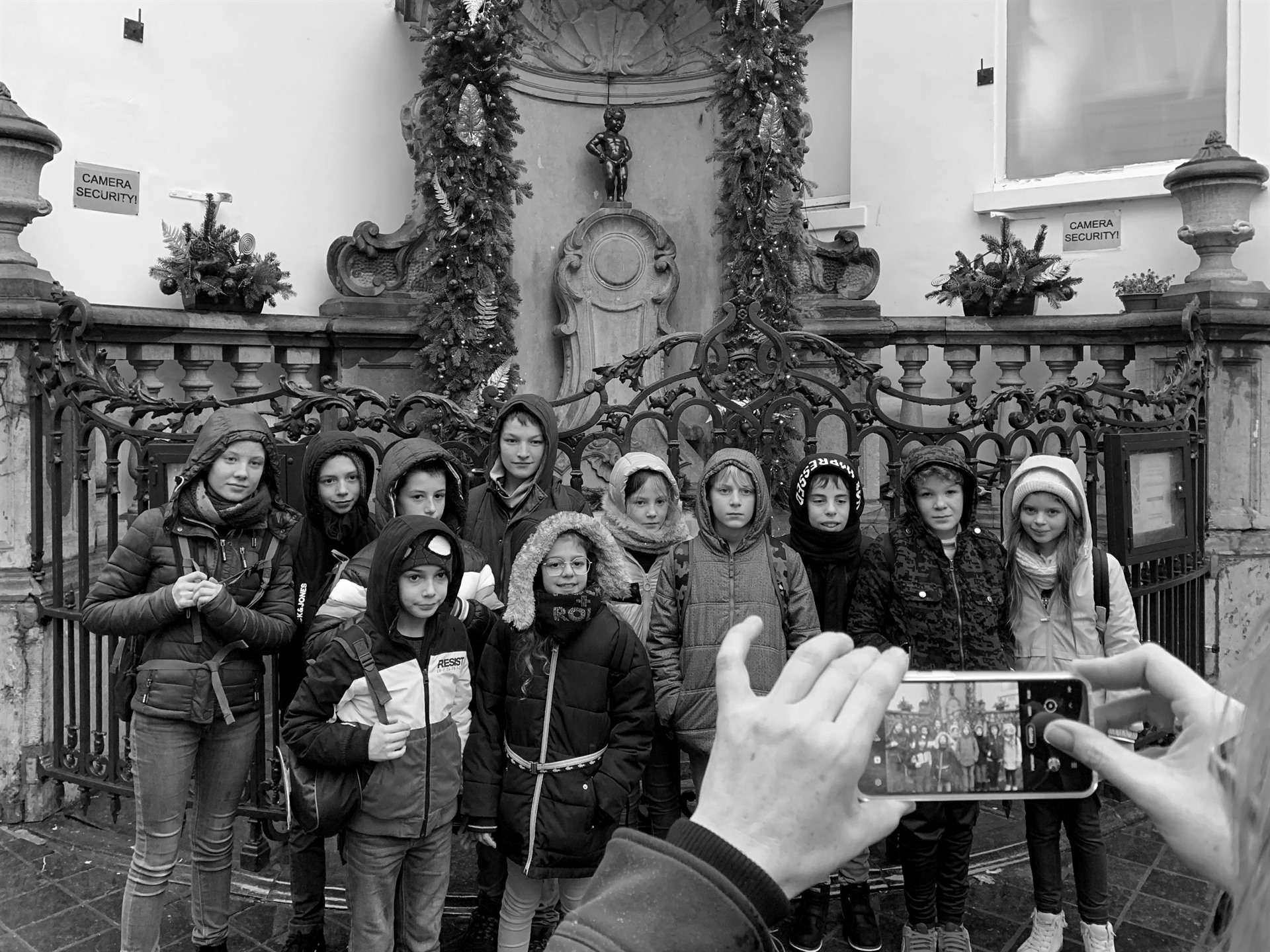 Children at Manneken Pis while someone photographs them with a smartphone.