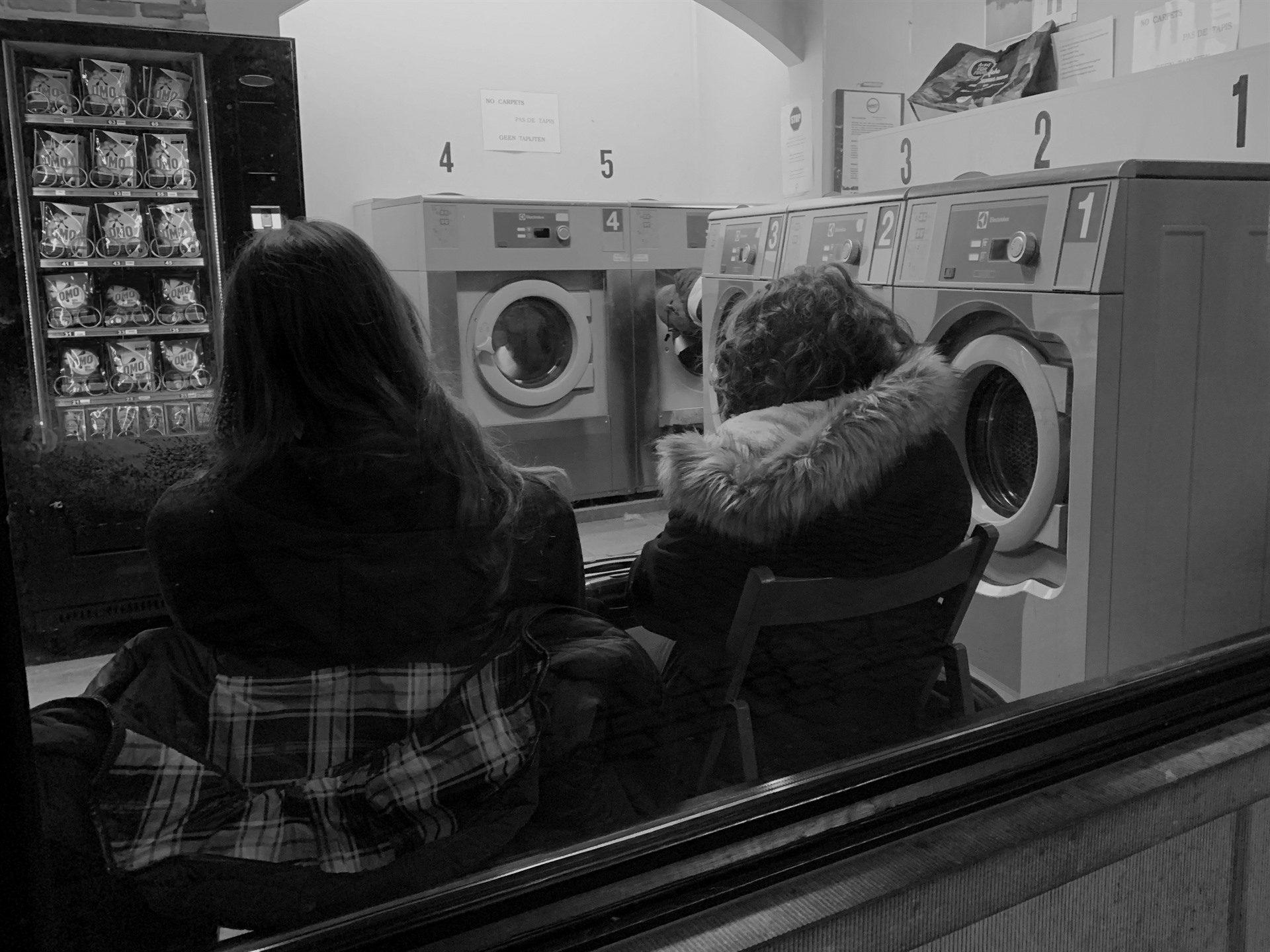 Two women seen from behind in a laundrette.