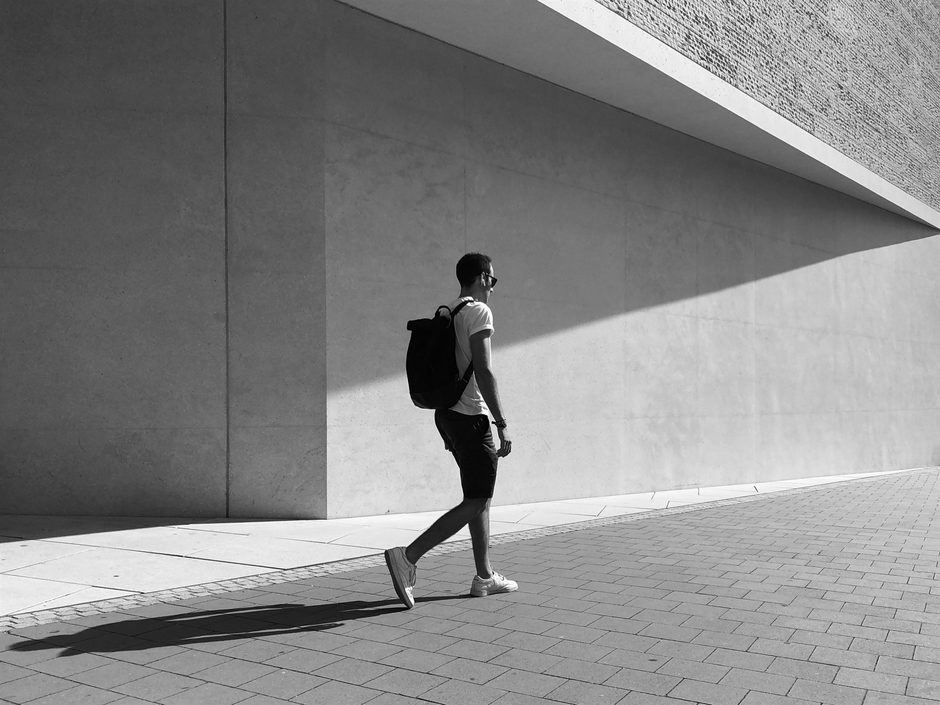Walking man with a large diagonal shadow on a concrete wall.