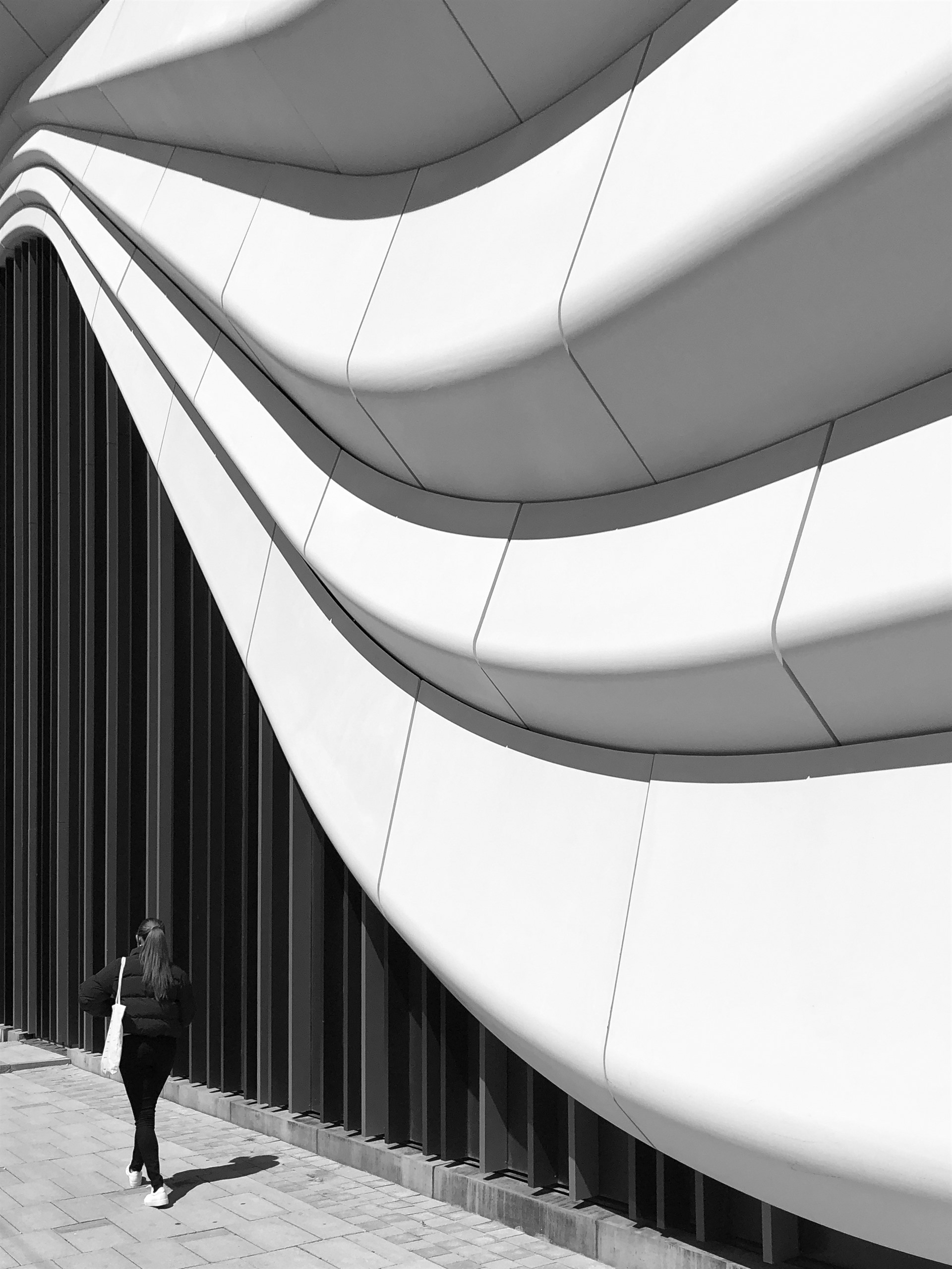 Woman beneath a large undulating modern facade.