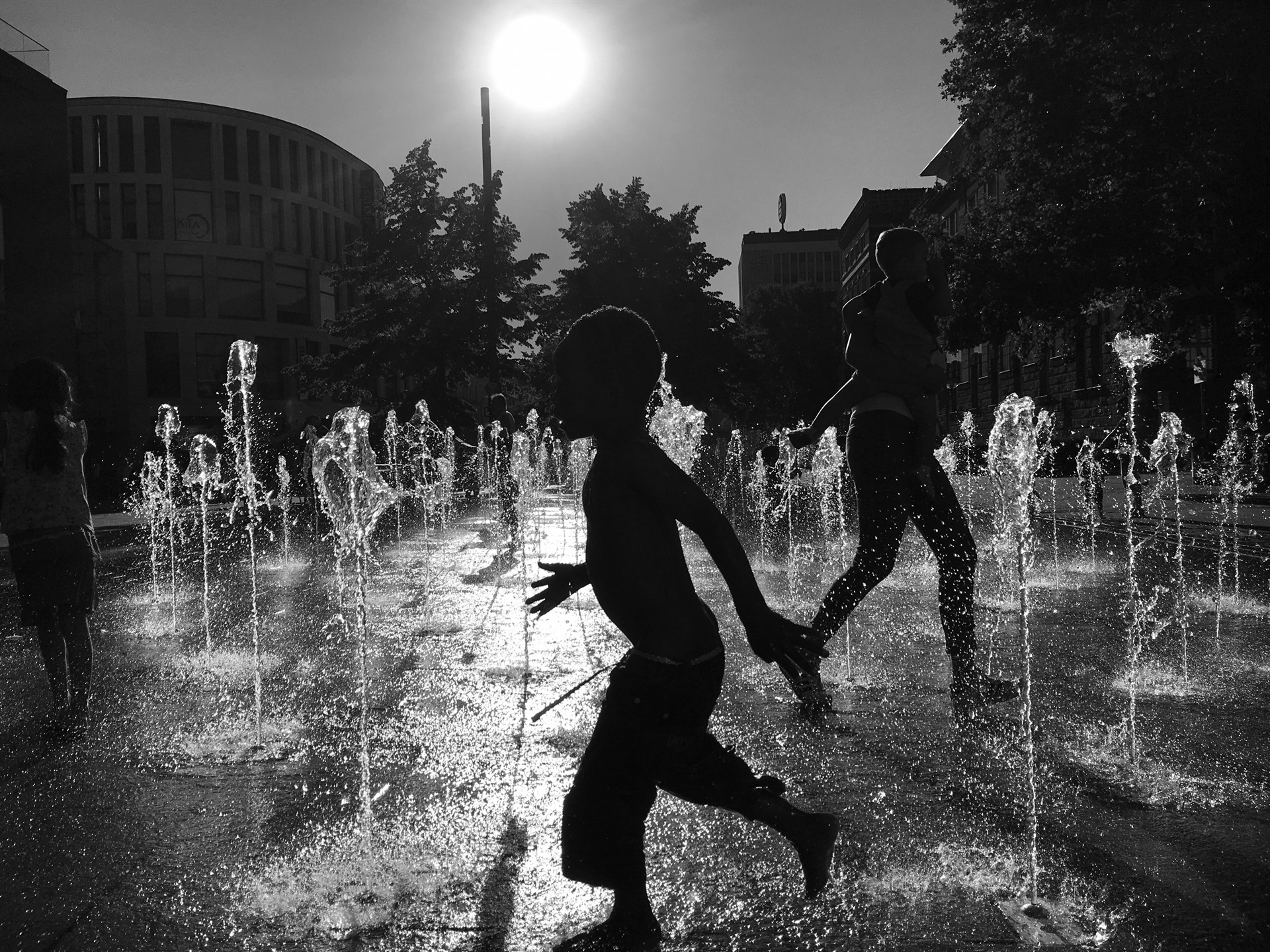 Running boy between fountains in strong backlight.