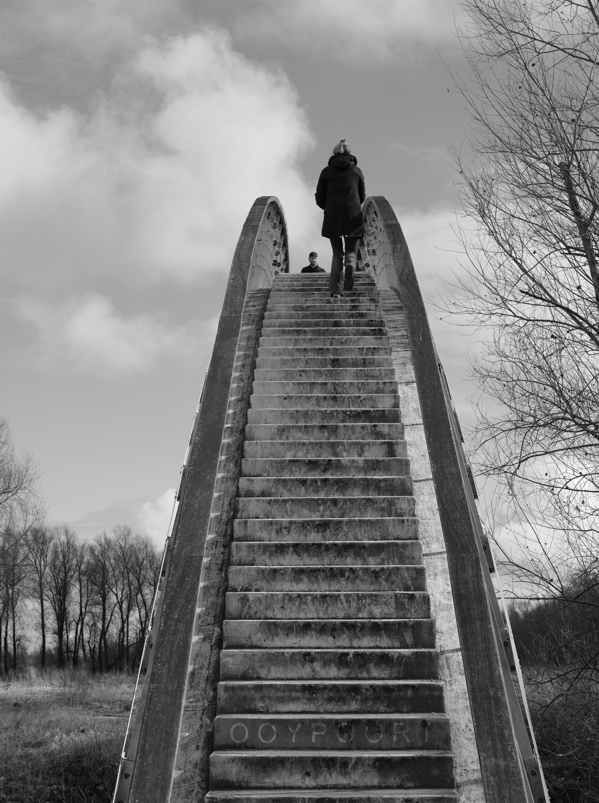 Woman at the top of a monumental curved bridge.