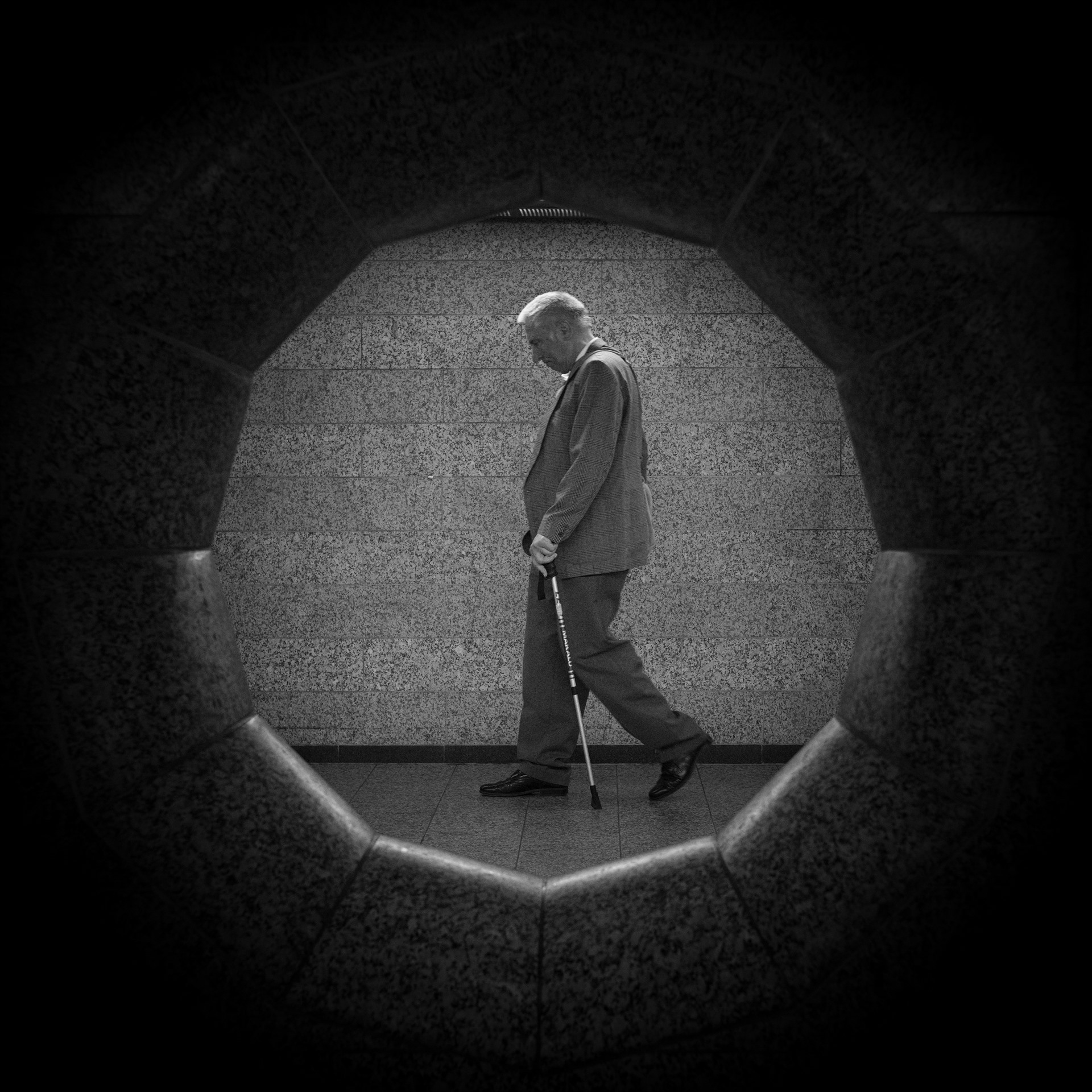 Man with a walking stick passing through a circular stone opening.