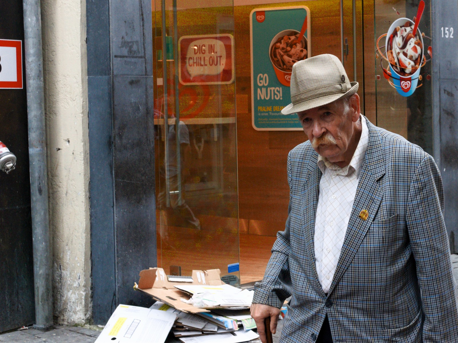 Older man reading a newspaper near a shop entrance.