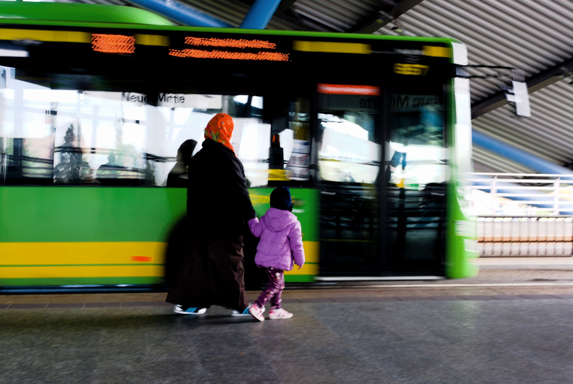 Dark and pink figures beside a green bus.