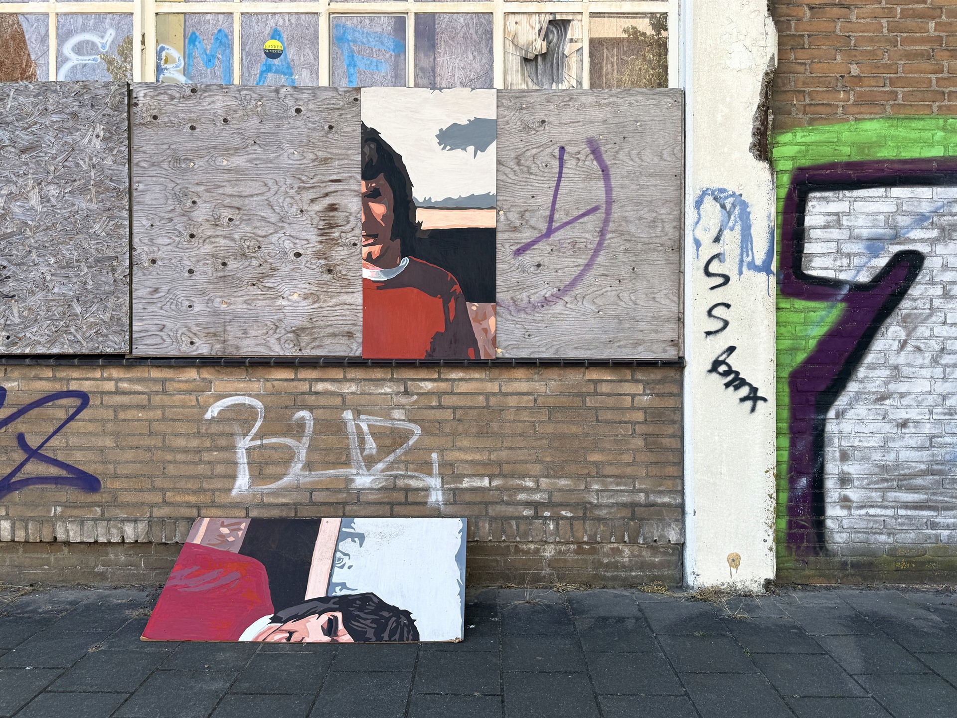 Painted panels and graffiti on a boarded-up brick facade.