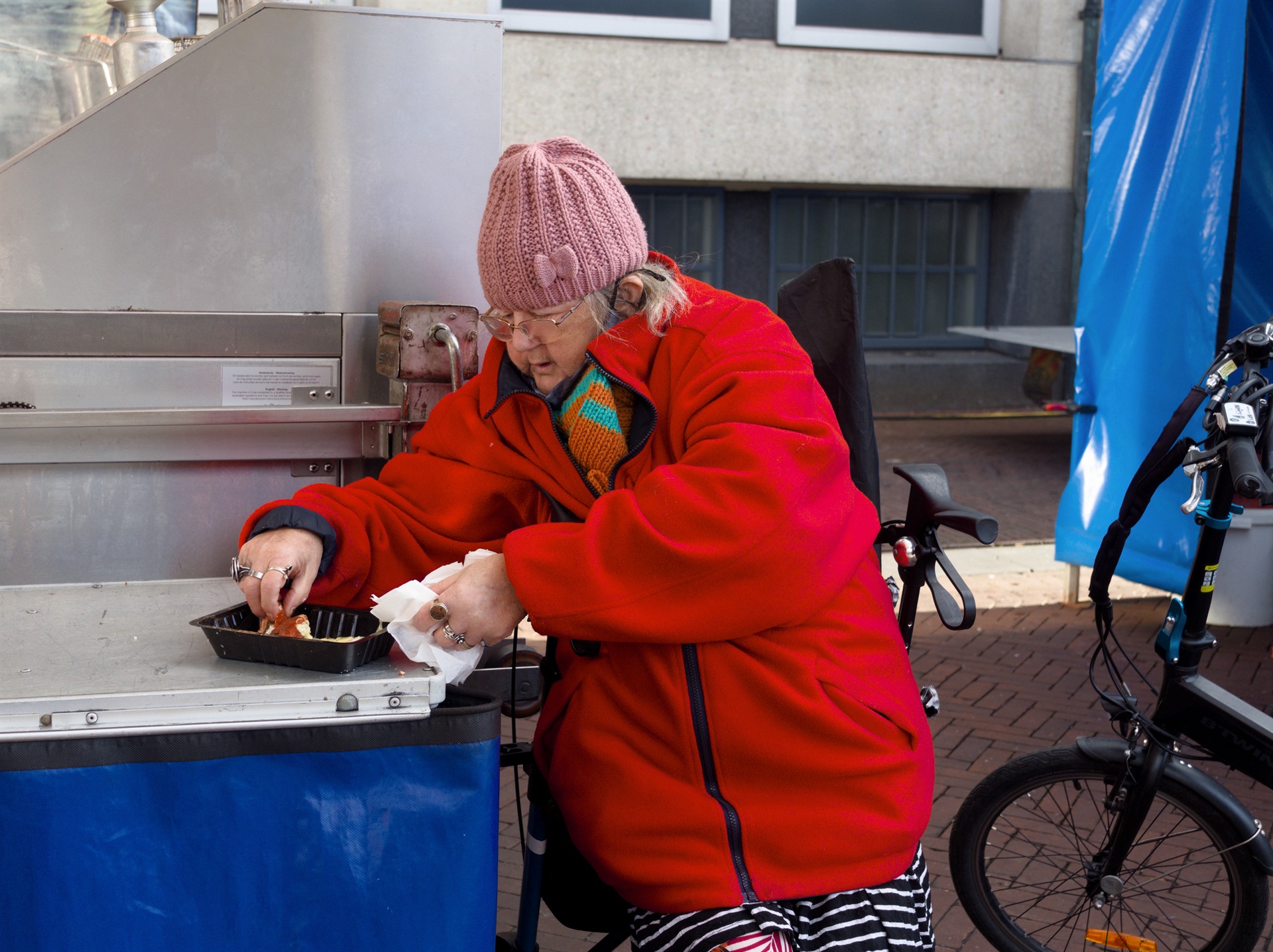 Older woman in a red jacket at a market stall.