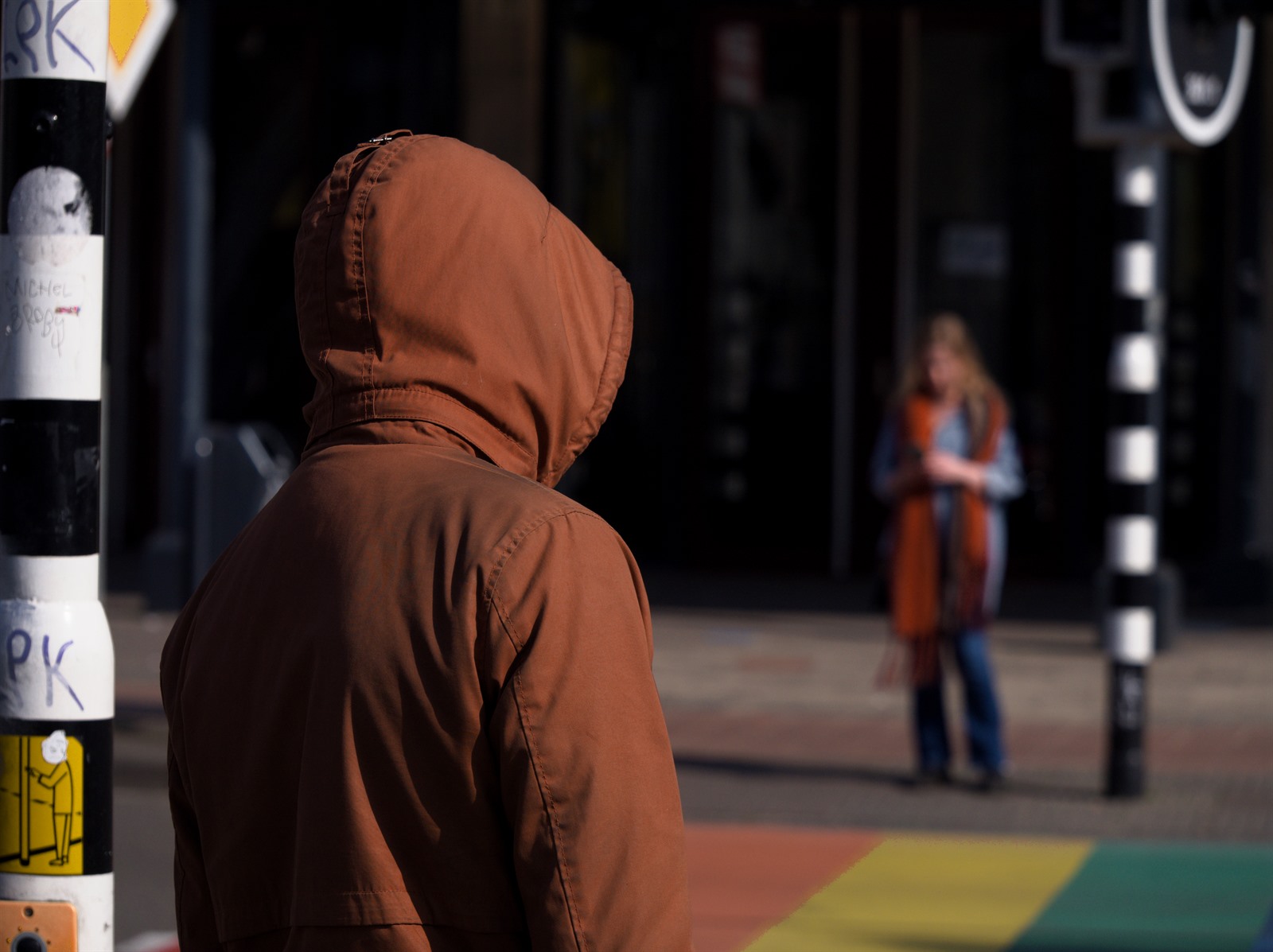 Figure in a brown hood against coloured planes.