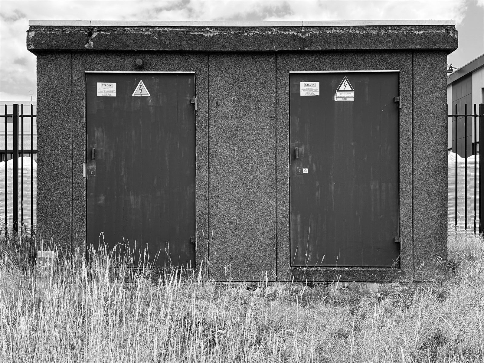 Two warning-marked doors on a small utility building surrounded by tall grass.