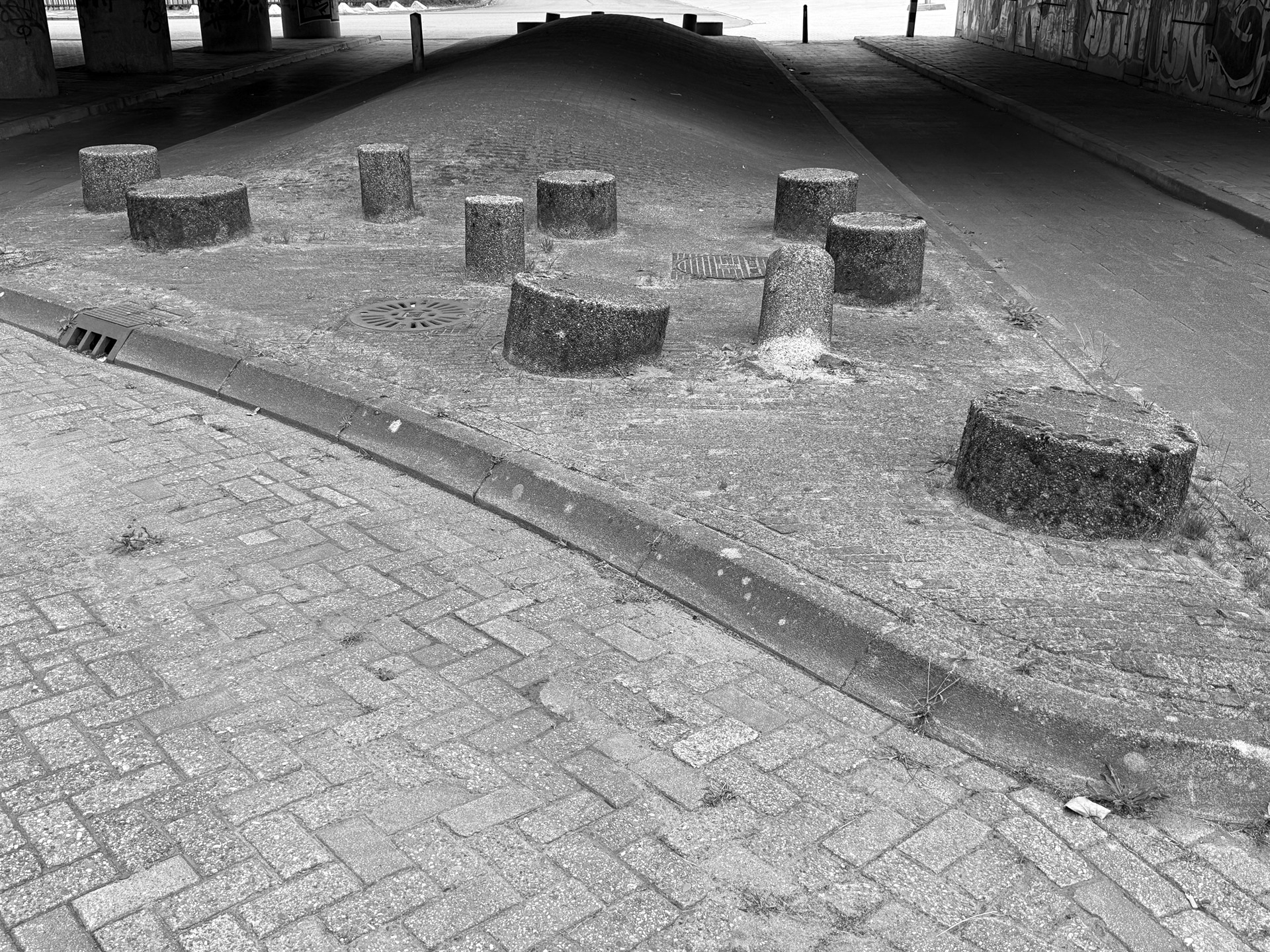 Cut concrete bollards scattered beside a curb beneath an overpass.