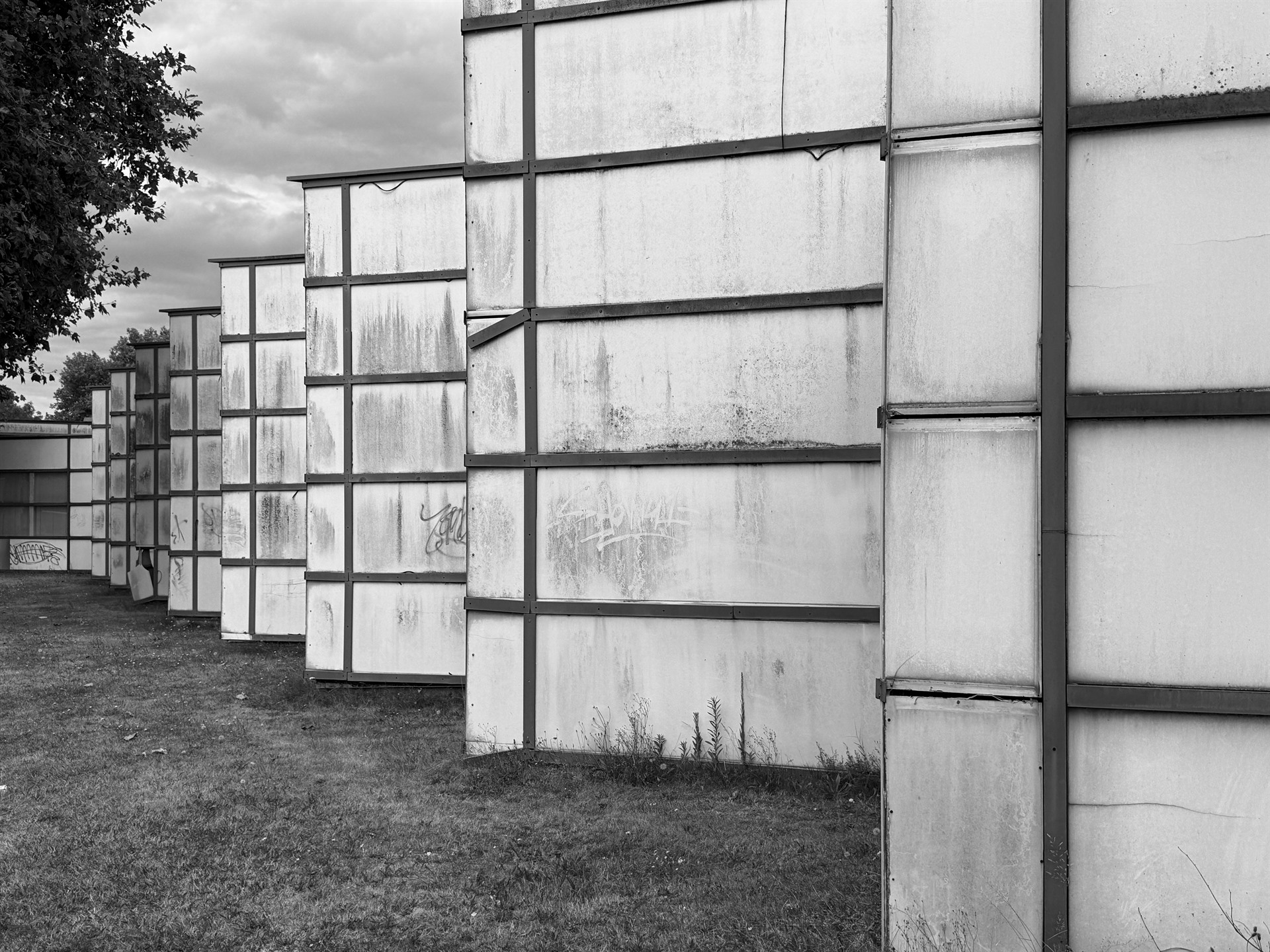 Row of weathered translucent industrial wall sections beside a strip of grass.